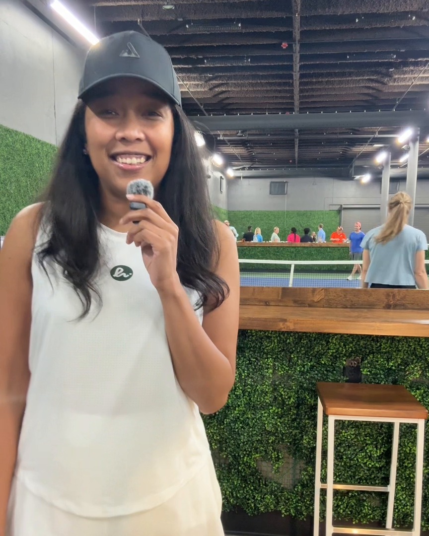 Lauren Bush actively hosting in a live venue with a handheld microphone.